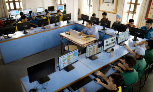 A group of students and a teacher at computers in a classroom.